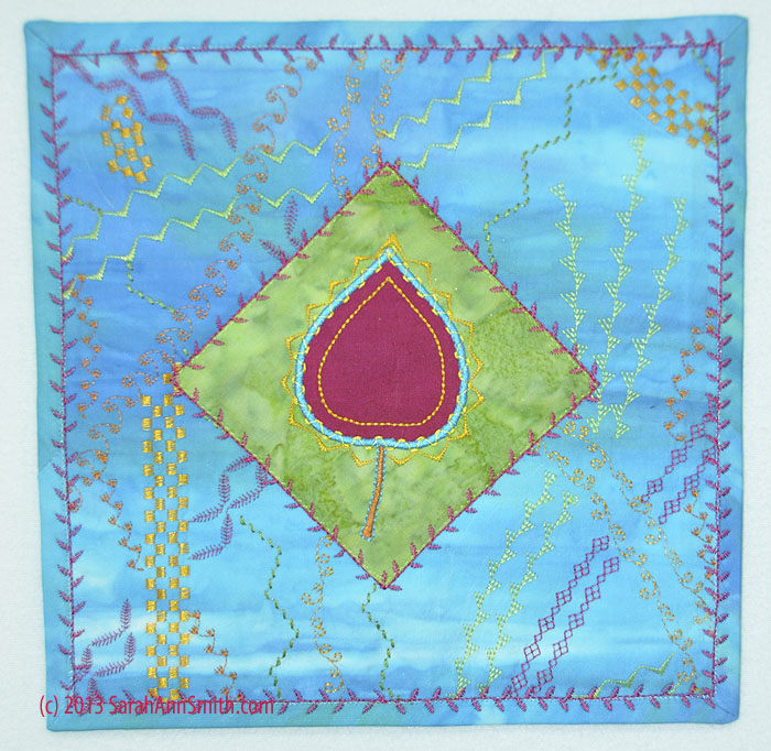 I made a smaller (about 9 inches square) quiltlet with the sampler leaf and the background stitching.  If you right click on this image, you can see more detail.  Notice how I layered up stitches to applique the green patch and how I used a decorative stitch on the binding.  On the latter, I used matching thread to machine stitch down the binding, then went over that with a decorative stitch.
